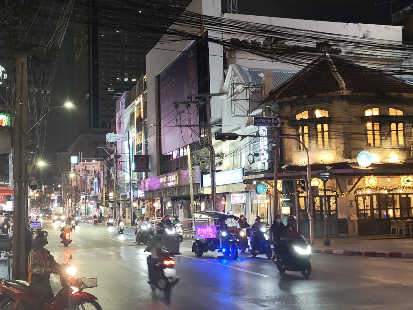 North Sathorn at night — tuk-tuk underlighting, a lit historic corner, overhead cable, a tower behind. The city is already running the systems; it just has not written them down.